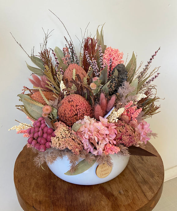 Wild Garden is created using dried, preserved and faux flowers and is displayed in a white ceramic squat pot. This natural arrangement using a variety of natives, fillers, eucalyptus and hydrangea is a perfect compact coffee table display Approx size is 30cm x 30cm including pot. Delivery Sutherland Shire. Delivery Sydney. Delivery Australia. Dried flower arrangement.